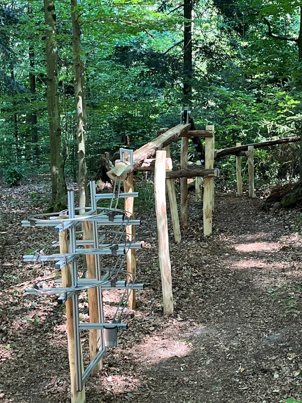 Metallwendel als Tempobremse, dahinter die geschnitzte Rinne auf Böcken – Waldmurmelbahn am Murrhardter Feenpfad
